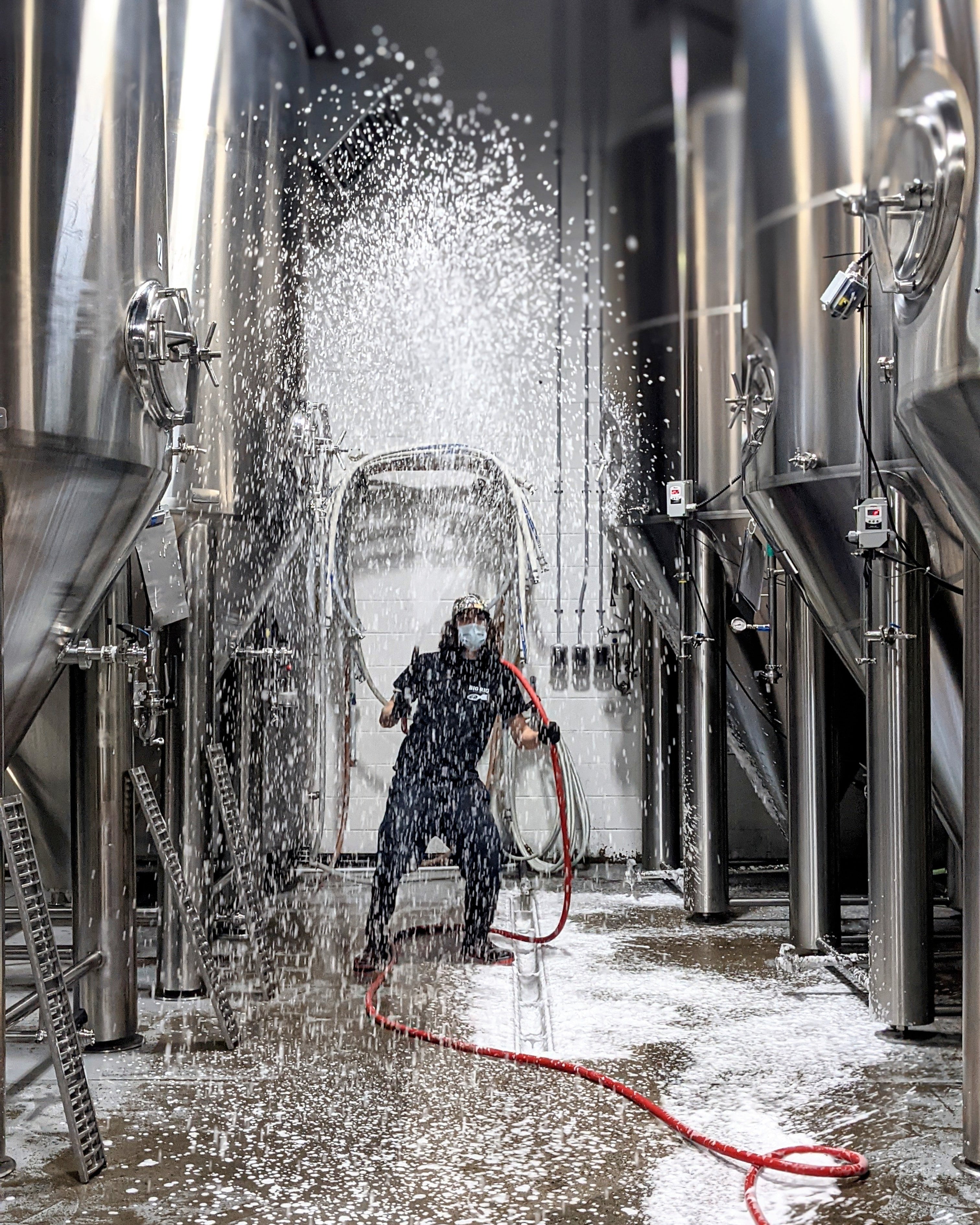Person cleaning large metal tanks with a hose in a brewery setting